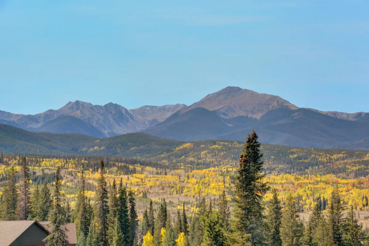A breathtaking view of a mountain range framed by colorful foliage and evergreen trees. The tranquil setting hints at opportunities for hiking and outdoor inspiration right outside the door.