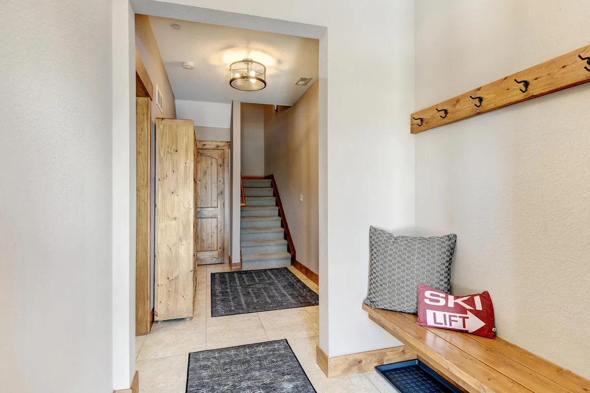 A welcoming entryway with a wooden bench, coat hooks, decorative pillows, and a staircase leading into the home. The scene creates a sense of immediate comfort and organization upon arrival back from outdoor activities.