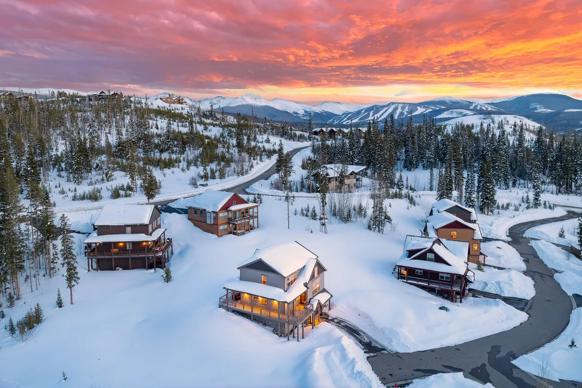 A serene winter scene with snow-covered houses against the backdrop of majestic mountains and a vibrant sunset. The image captures both the serenity and excitement of mountain living, hinting at après-work relaxation and scenic surroundings.