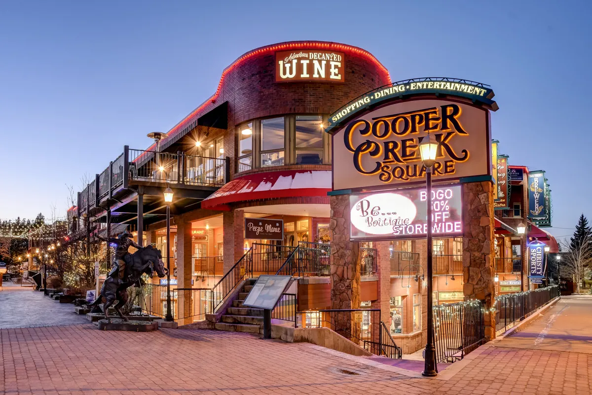The lively exterior of Cooper Creek Square featuring shopping, dining, outdoor seating, and event signage. The festive atmosphere suggests easy access to local amenities, cafes, and entertainment just minutes away.