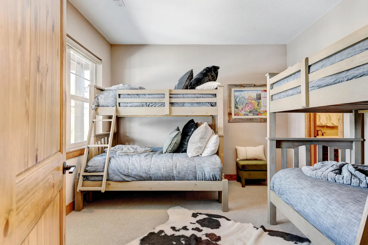 A playful yet inviting bunk room is featured in this image, with two bunk beds dressed in plush pillows and cheerful bedding. Artwork on the wall and a soft ambiance make this space ideal for kids or siblings, offering both comfort and a whimsical touch.