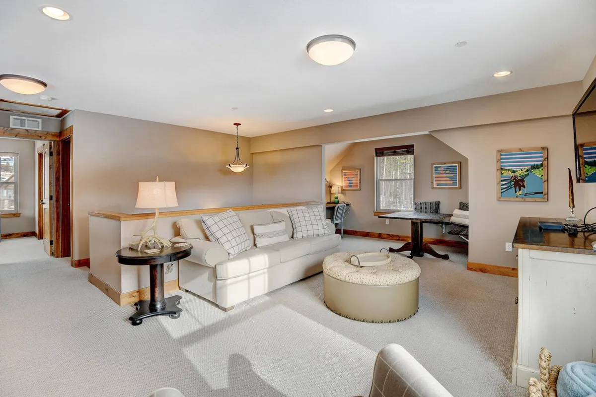 A bright loft space with a comfortable sofa, practical desk area, coffee table, and art on the walls. The loft is airy and designed for both work and relaxation, supporting remote work or quiet reading as well as casual lounging.